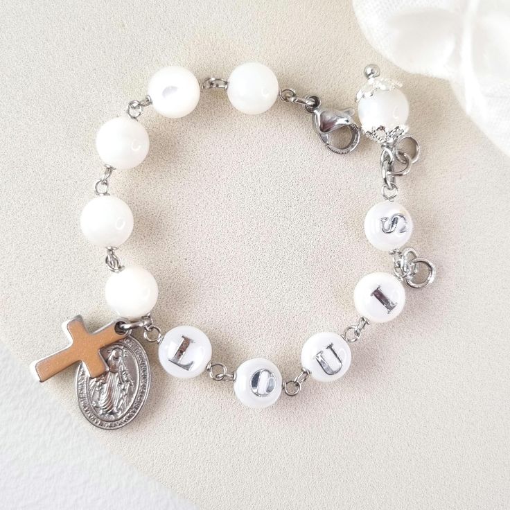 This stunning Baptism bracelet is a truly divine piece that combines elegance and spiritual significance. Crafted with natural mother of pearl beads, it features gold plated virgin Mary and cross charms that symbolize protection and faith. The bracelet is personalized with a handcrafted initial letter, adding a unique touch to this meaningful piece. Perfect for commemorating a special occasion or as a thoughtful gift, this bracelet is a beautiful reminder of faith and blessings. *MATCHING ROSARY PRAYER: https://www.etsy.com/au/listing/1492666531/personalized-rosary-beads-pearl-rosary *Materials:  High Quality 18k gold plated Stainless Steel charms * Gemstone: Genuine mother of pearl beads, round shape, 6mm * Closure: adjustable finial, lobster clasp * Letter beads: handmade, mother of pear White Name Bracelets For Wedding, Personalized White Bracelets For Wedding, White Hypoallergenic Pearl Bracelet For First Communion, Hypoallergenic White Pearl Bracelet For First Communion, Adjustable White Name Bracelet Nickel Free, Adjustable Nickel-free White Name Bracelet, White Engraved Bracelets For Personalized Gift, Adjustable White Nickel-free Name Bracelet, Personalized White Engraved Bracelets