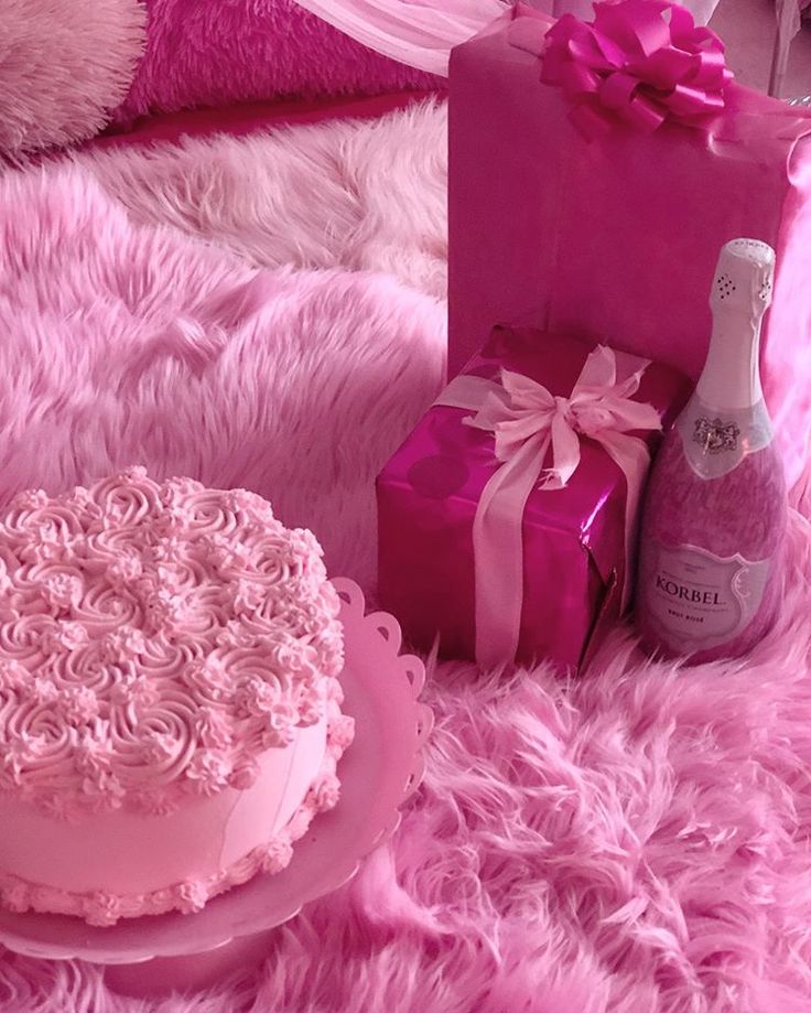 a pink cake, bottle of champagne and gift bags on a fluffy blanket with fur