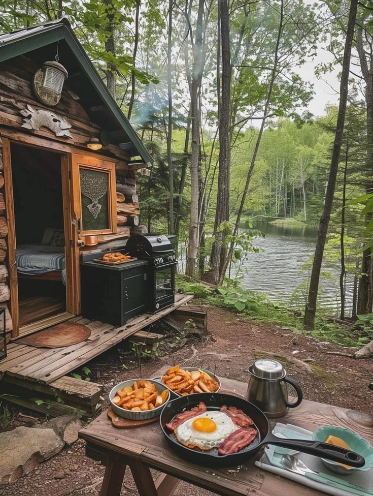 a table with food on it next to a small cabin in the woods near a lake