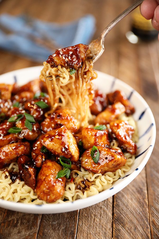 someone is eating some noodles with chicken and sauce on top, while holding a fork