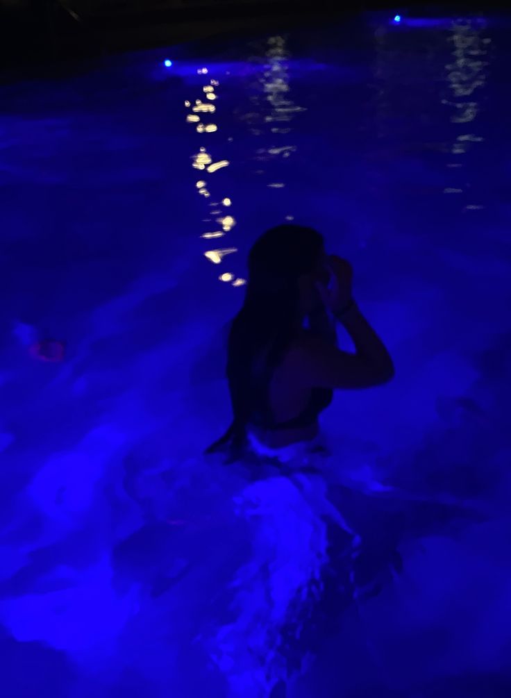 a woman sitting in the middle of a pool talking on her cell phone at night