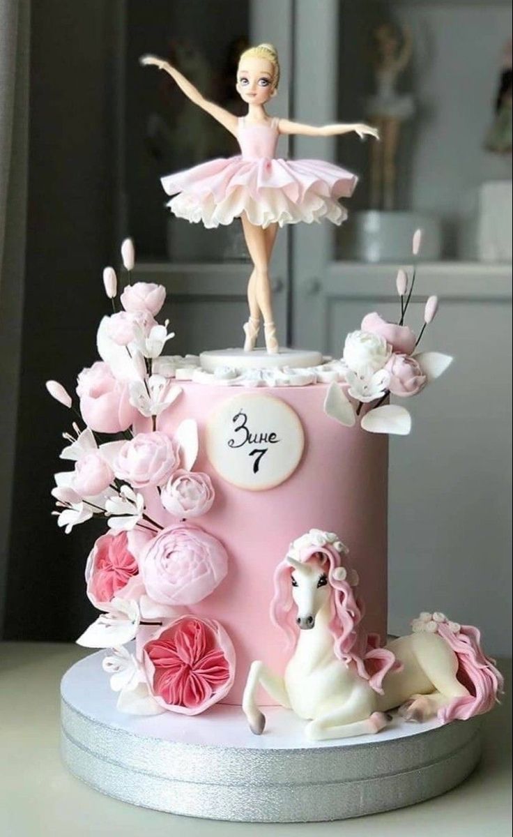 a pink cake with a barbie doll on top and flowers around the base, as well as a horse figurine