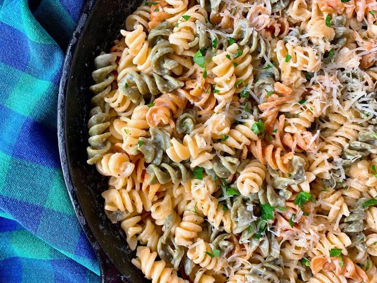 a skillet filled with pasta and vegetables on top of a blue towel next to a fork