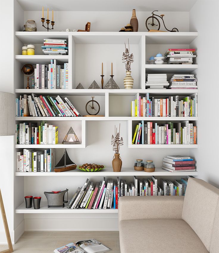 a white book shelf filled with lots of books next to a beige chair and lamp