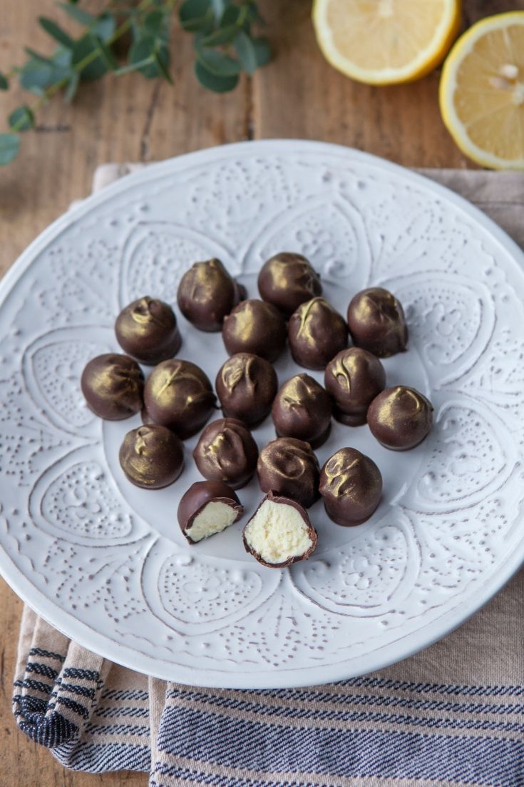 a white plate topped with chocolate covered candies next to sliced lemons on a wooden table