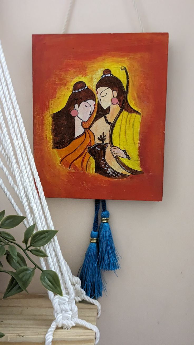 a painting hanging on the wall next to a potted plant and white rope with blue tassels