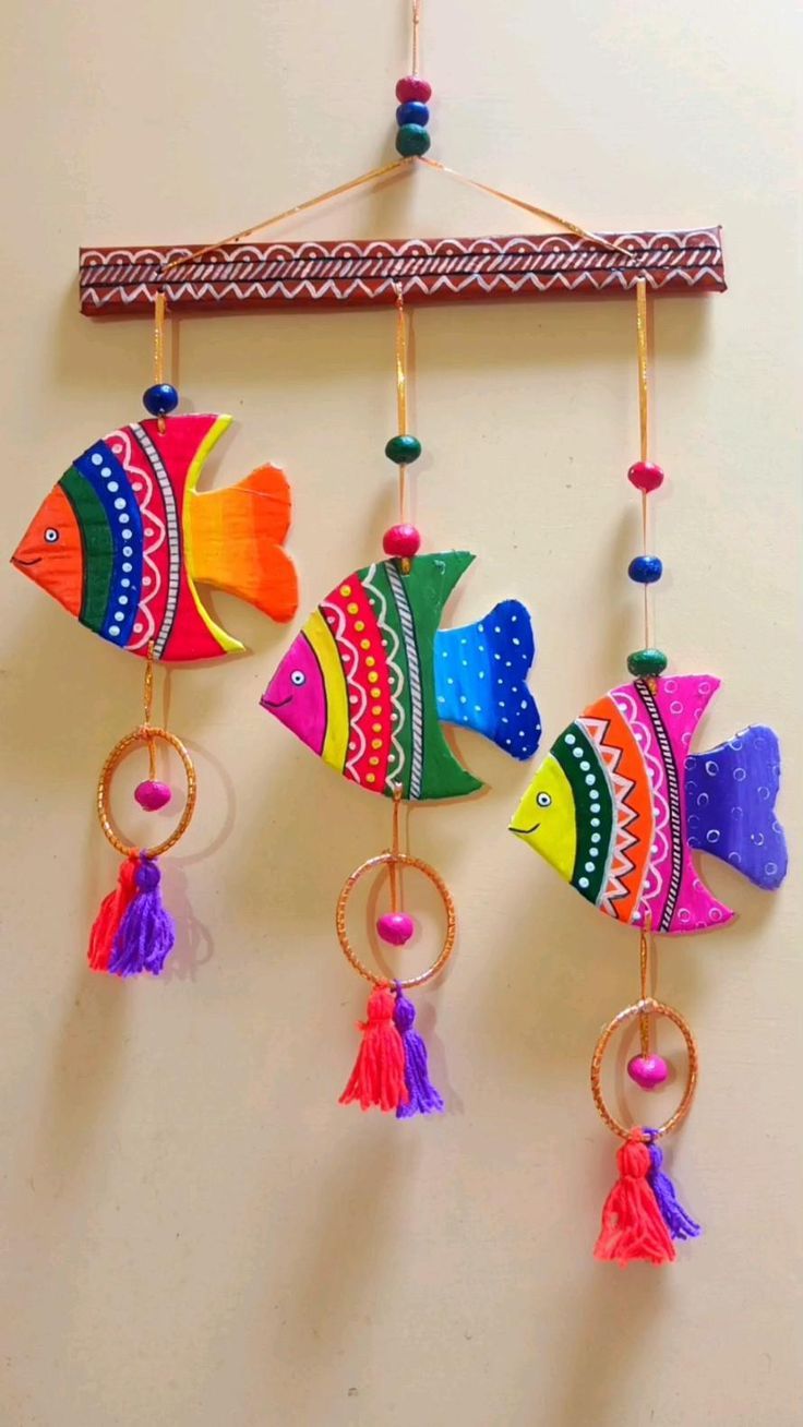 three colorful fish hanging on a wall with tassels attached to the hooks,