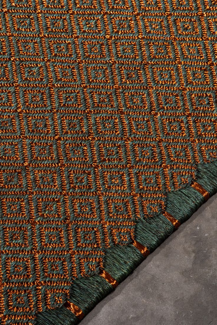 an orange and green rug with fringes on the bottom, in front of a concrete floor