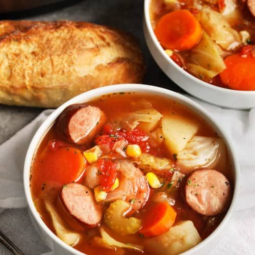 two white bowls filled with soup next to a loaf of baguette bread on a table