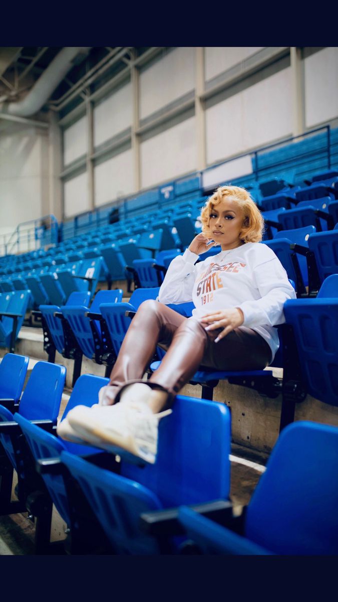 a woman sitting in the middle of a blue stadium seat with her legs crossed and head resting on her hand