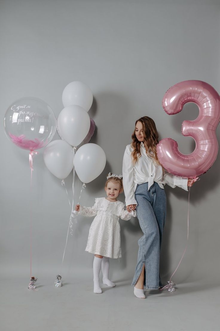 a mother and daughter holding balloons in front of the number three