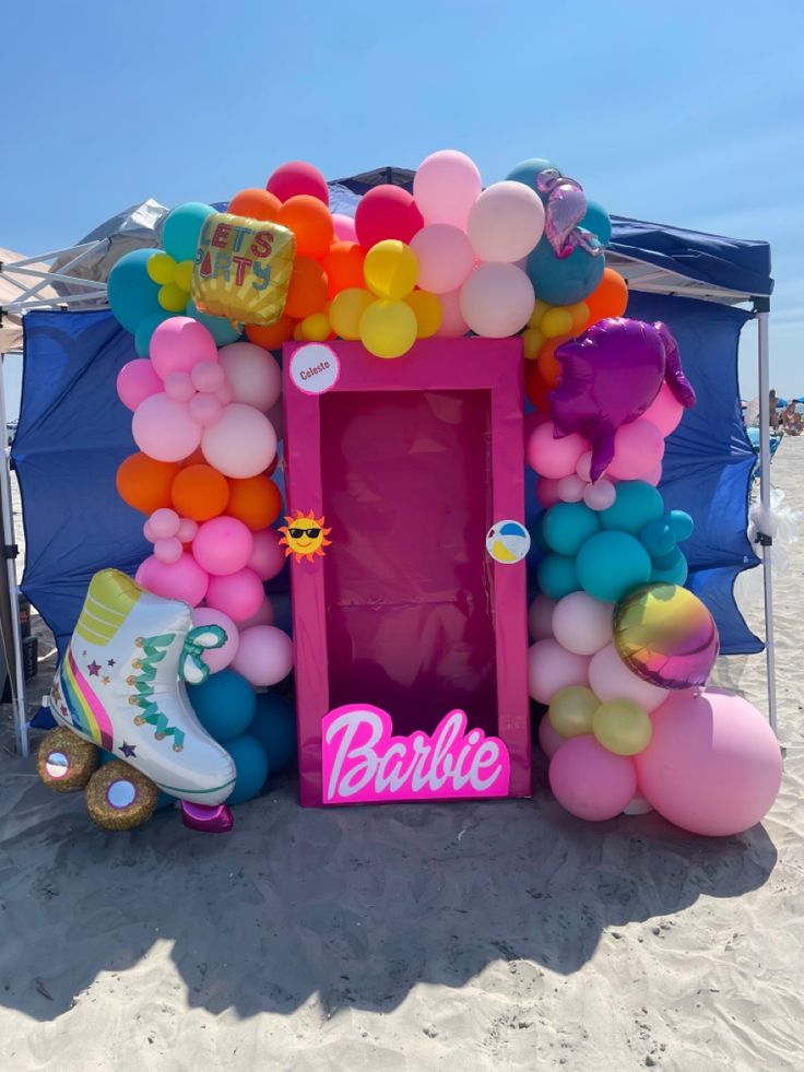 a pink door with balloons and shoes on the beach next to an arch that says barbie