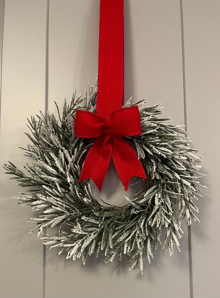 a christmas wreath hanging on a door with a red ribbon and bow around the front