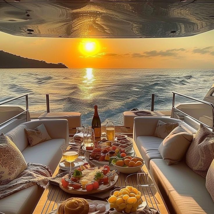 a table with food and drinks on it in front of the sun setting over the ocean