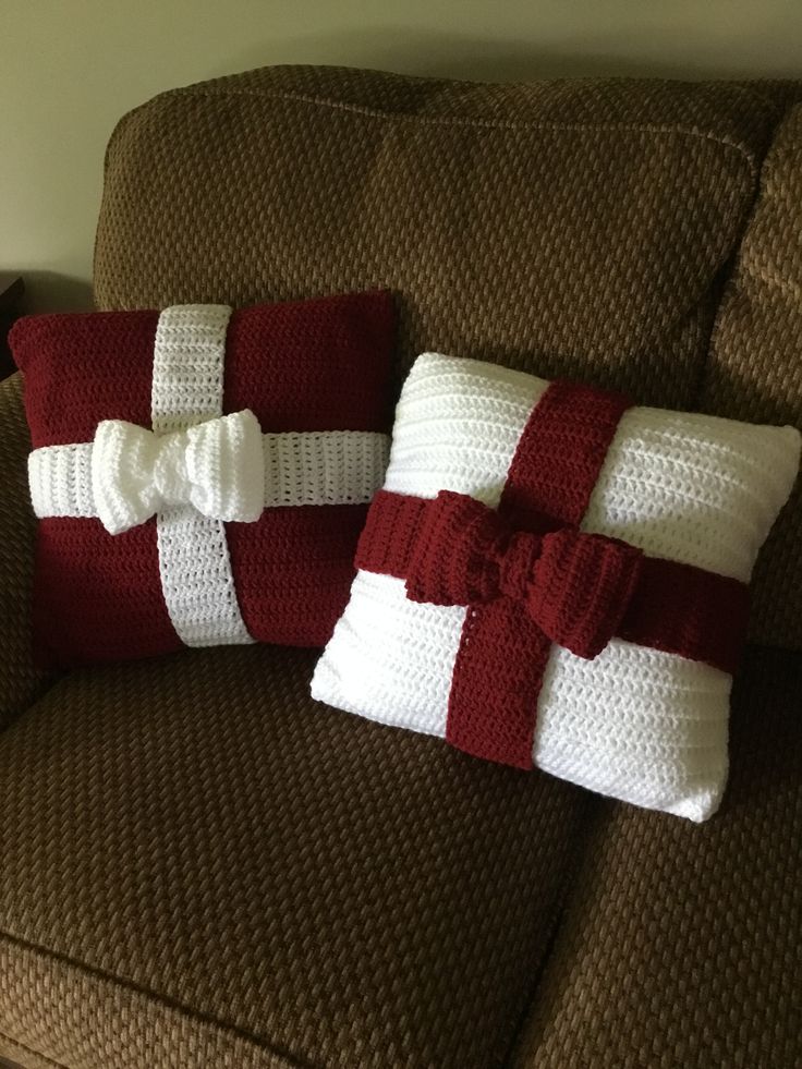 two red and white knitted pillows on a brown couch with bows tied around them