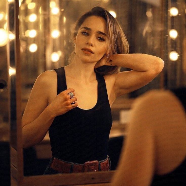 a woman is standing in front of a mirror with her hand on her head and looking into the mirror