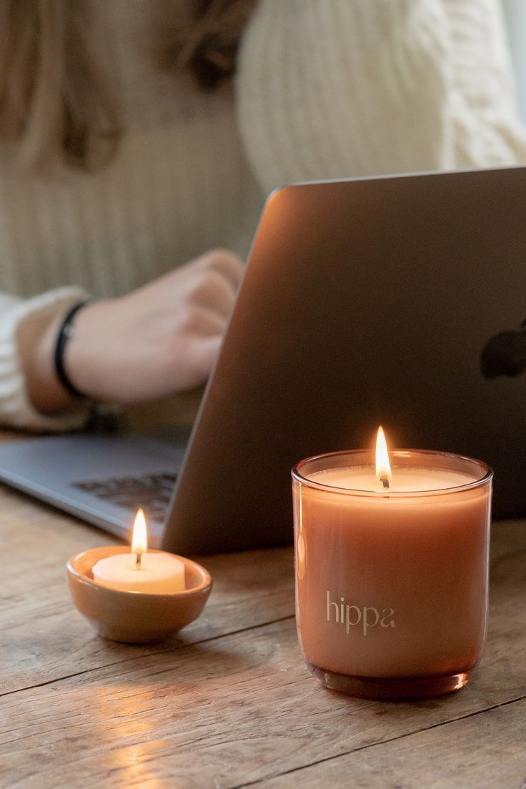 a candle sitting next to a laptop on a wooden table in front of a woman