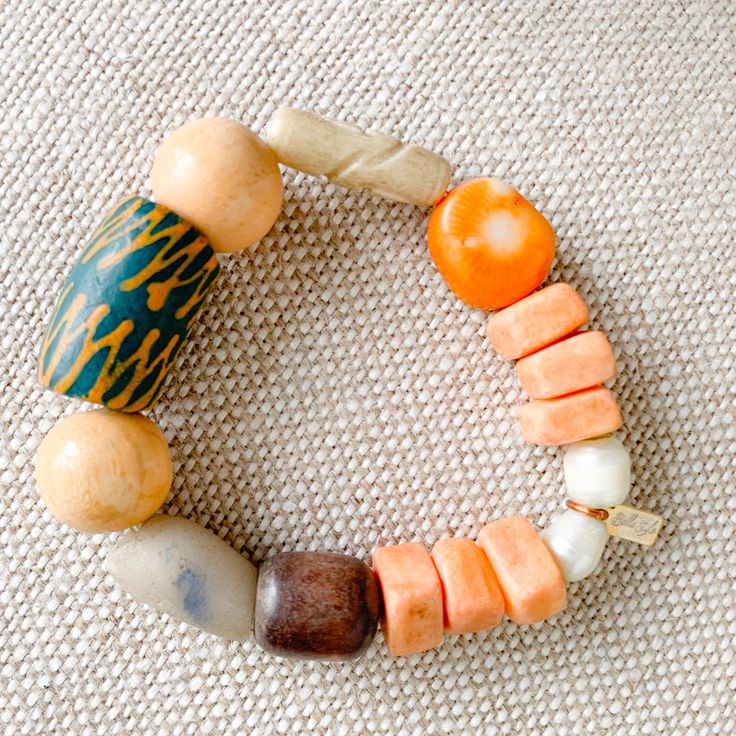 Sustainable Bracelet. A bright bold green hand painted prayer bead with neutral rosewood and soft peach beads. African prayer beads from Africa’s Ivory Coast for loyalty, love and health. Featuires orange coral stone. Rosewood from the tree of health and wisdom. Freshwater large pearls in mint. Sterling silver BelleStyle logo tag. Comes in linen travel pouch. One of a kind. Made in USA. Handmade Spiritual Orange Stretch Bracelet, Spiritual Wooden Beads Stretch Bracelet For Healing, Artisan Wooden Beads Bracelets For Meditation, Orange Stretch Bracelet With Large Beads As Gift, Earthy Wooden Beaded Bracelets As Gift, Gift Orange Stretch Bracelet With Large Beads, Earthy Wooden Beaded Bracelets For Gift, Artisan Wooden Beads Bracelet For Meditation, Multicolor Large Beaded Bracelets For Meditation