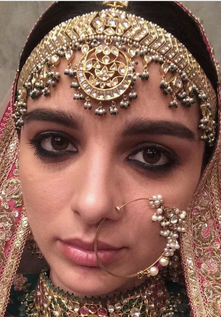 a woman wearing an elaborate head piece and veil with jewels on her face, looking at the camera