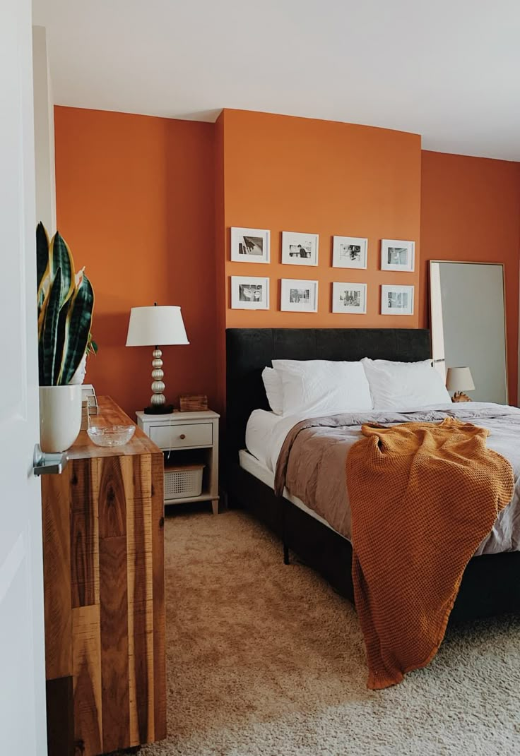 a bedroom with an orange accent wall and white bedding is pictured in this image