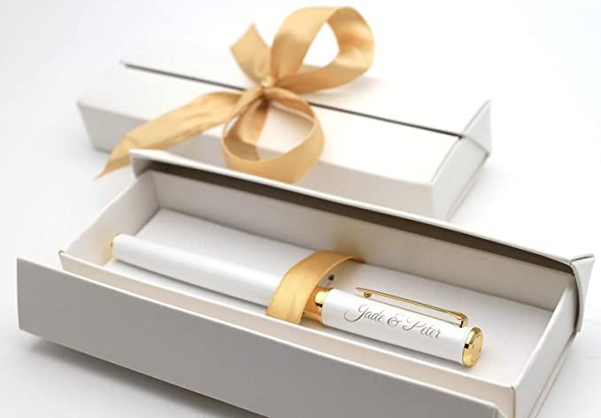 a white box with a gold ribbon around it and a pen in the bottom one