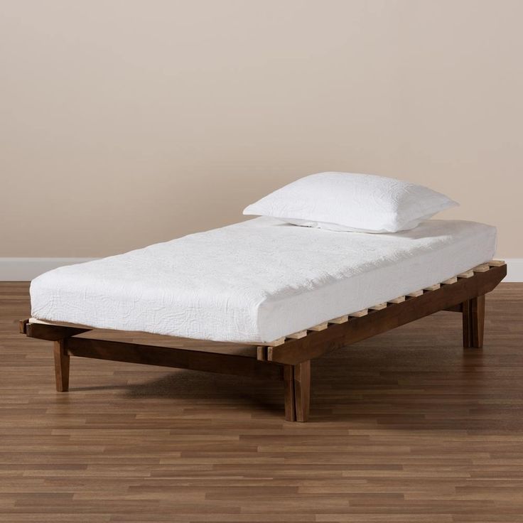 a small bed with white sheets and pillows on it in a room that has hardwood floors