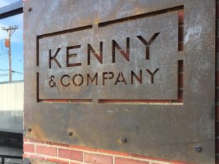 a sign on the side of a building that says kenny & company and is attached to a brick wall