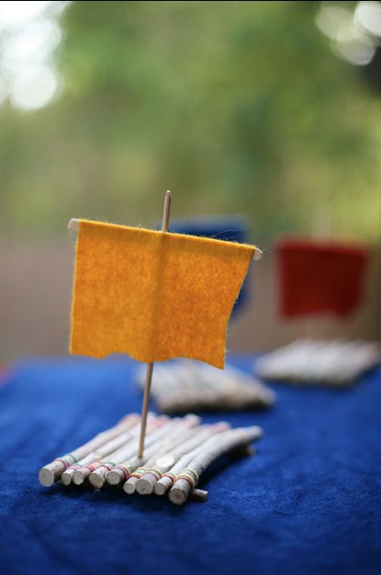 a small yellow sail boat on top of blue cloth next to metal rods and wood sticks