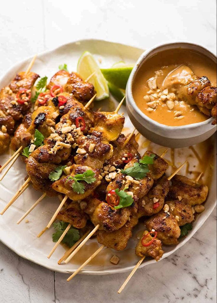 chicken skewers with peanut sauce and garnish on a white platter