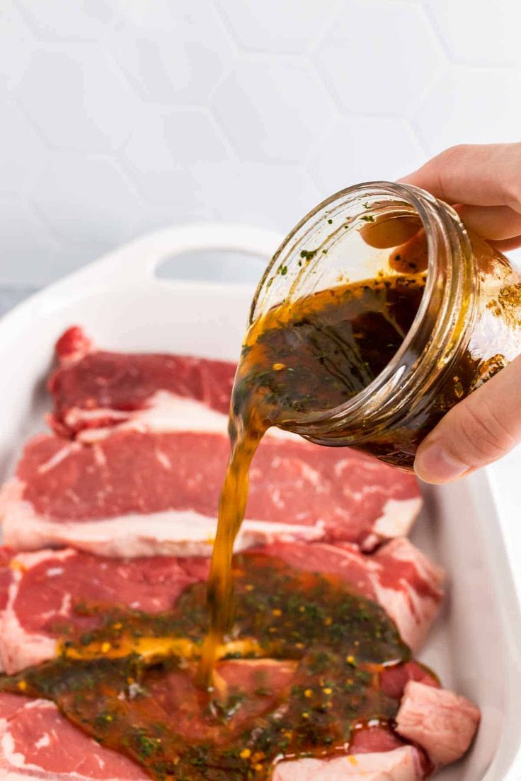 someone pouring sauce on raw meat in a white dish