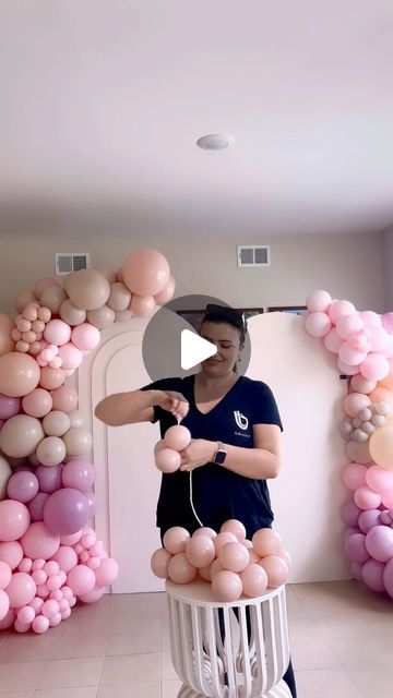 a woman is standing in front of balloons on the wall and making a balloon arch