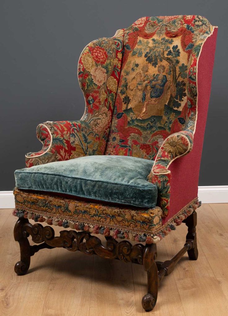 an ornately decorated chair with blue velvet upholstered back and foot rests against a gray wall