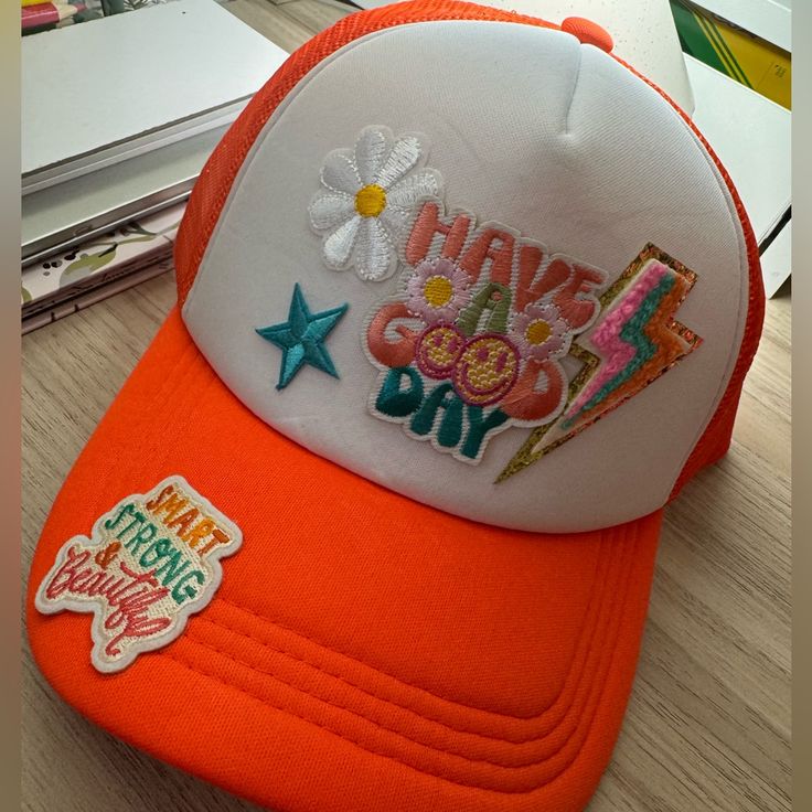 an orange and white hat that says have good day with flowers on the front, sitting next to a laptop