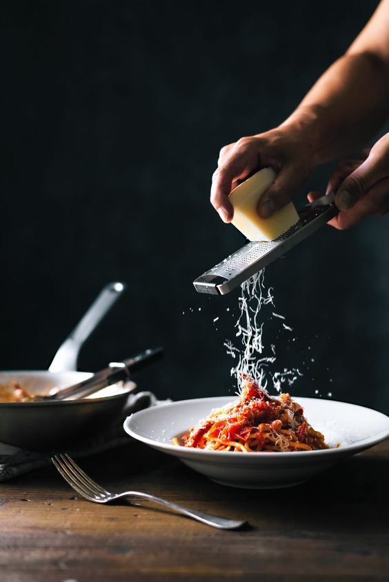 a person is sprinkling cheese on top of a plate of spaghetti and sauce