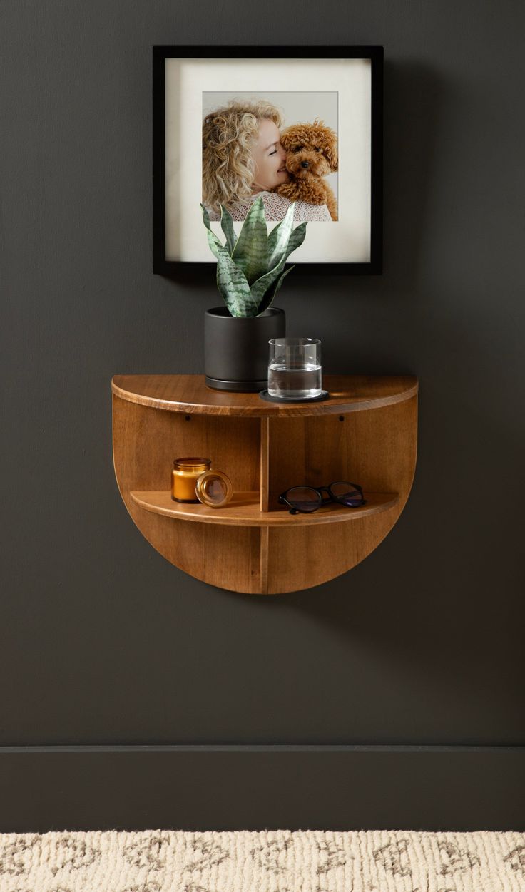 a wooden shelf with a potted plant on top of it next to a framed photo