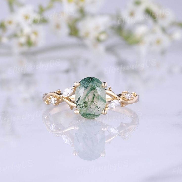 a ring with a green stone in it on a white table next to some flowers