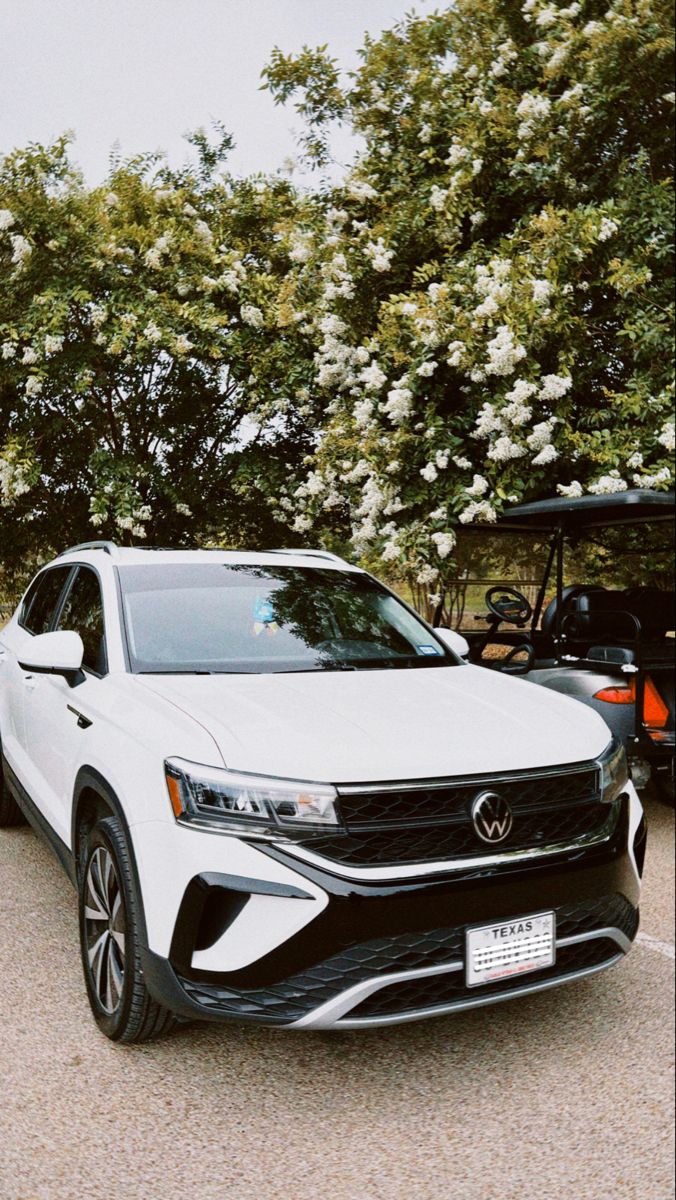 a white car parked next to a golf cart in a parking lot with flowers on the trees