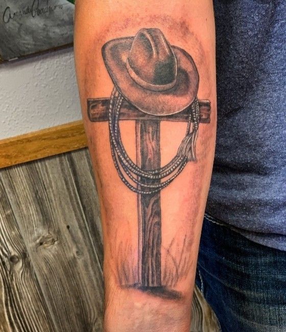 a man's arm with a cowboy hat and lasso on the cross tattoo