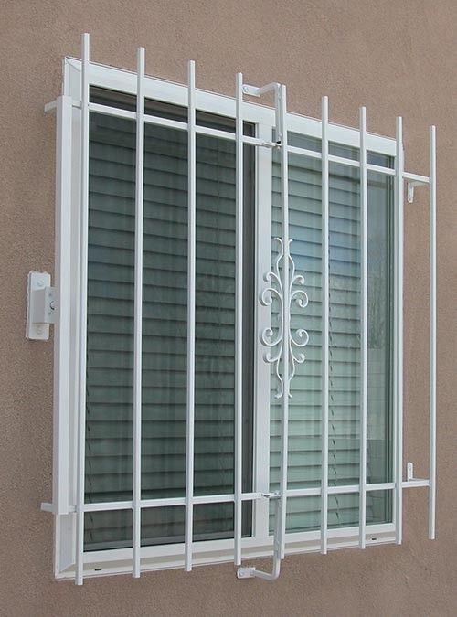 a white window with bars on the side of it next to a wall and a building