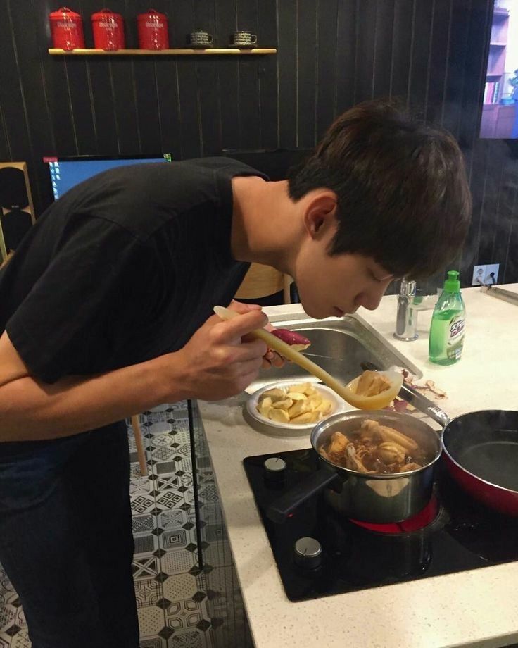 a young man preparing food on top of a stove next to a pot and pan