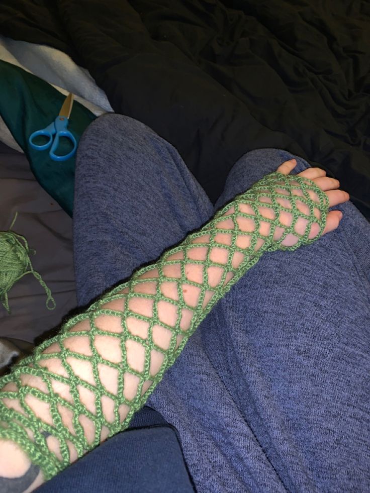 a person wearing green knitted arm warmers with scissors on their feet next to them