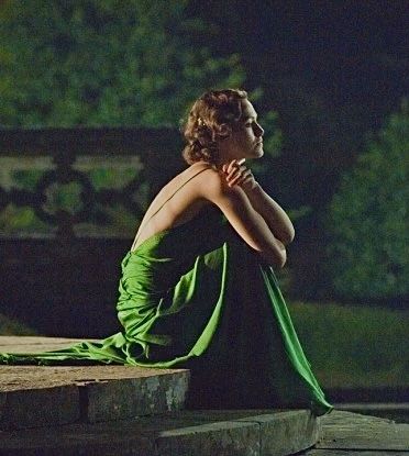 a woman in a green dress is sitting on the edge of a stone wall with her hand under her chin