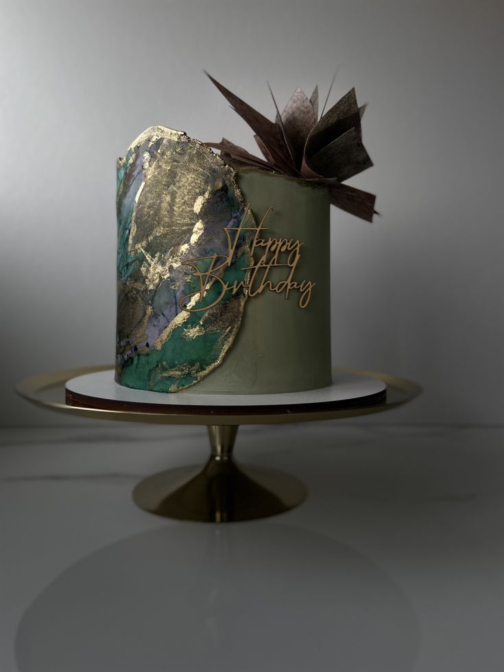 a green and gold birthday cake sitting on top of a white plate with a brown bow