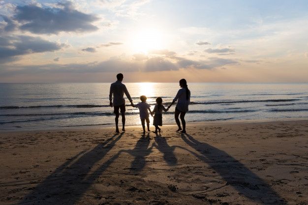 a family standing on the beach at sunset with their shadow cast by the sun's rays