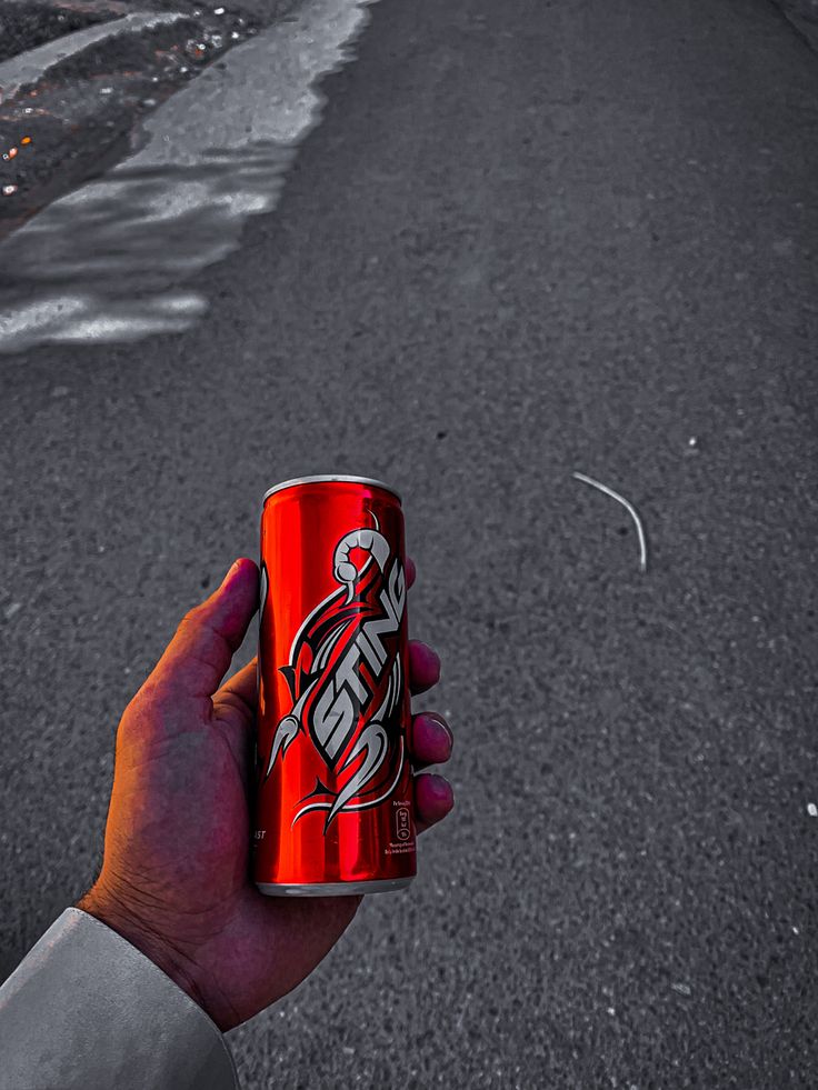 a person holding up a can of soda on the side of an empty city street