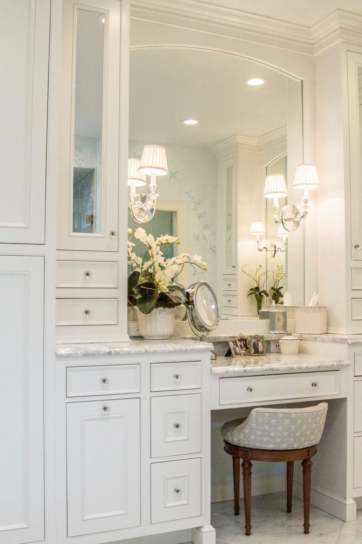 a bathroom with white cabinets and marble counter tops, along with a stool in front of the mirror