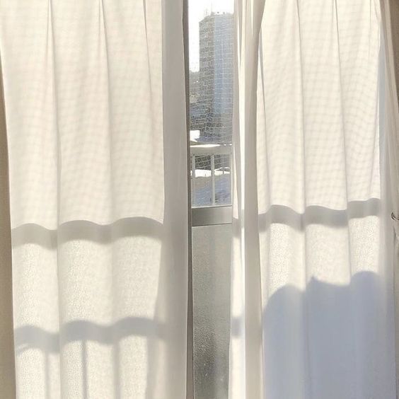 a cat sitting on top of a window sill in front of a white curtain