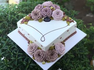 a heart shaped cake decorated with flowers on top of a white plate in front of some bushes