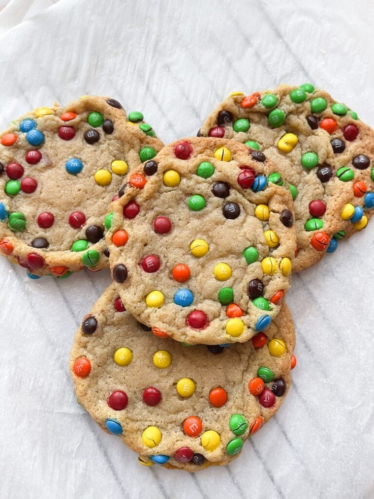 three cookies with m & m's and chocolate chips are on a white napkin