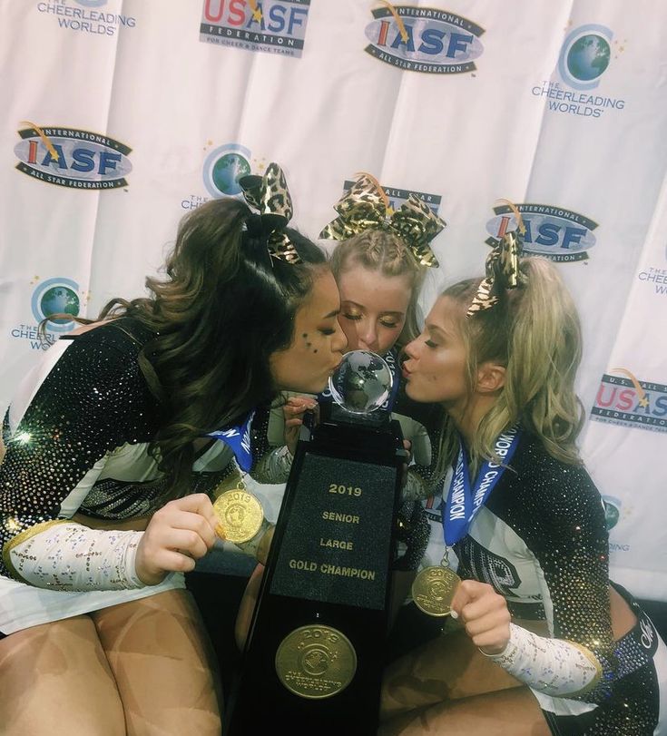 three women kissing each other while sitting on the floor in front of a wall holding a trophy